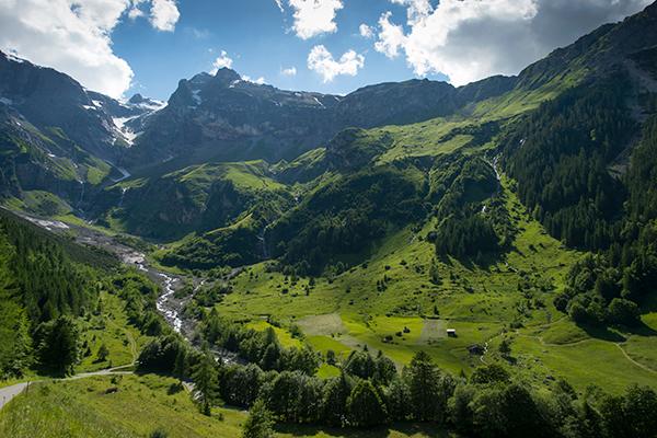 Berglandschaft mit Gebirgsfluss, grüne Wiesen und blauer Himmel